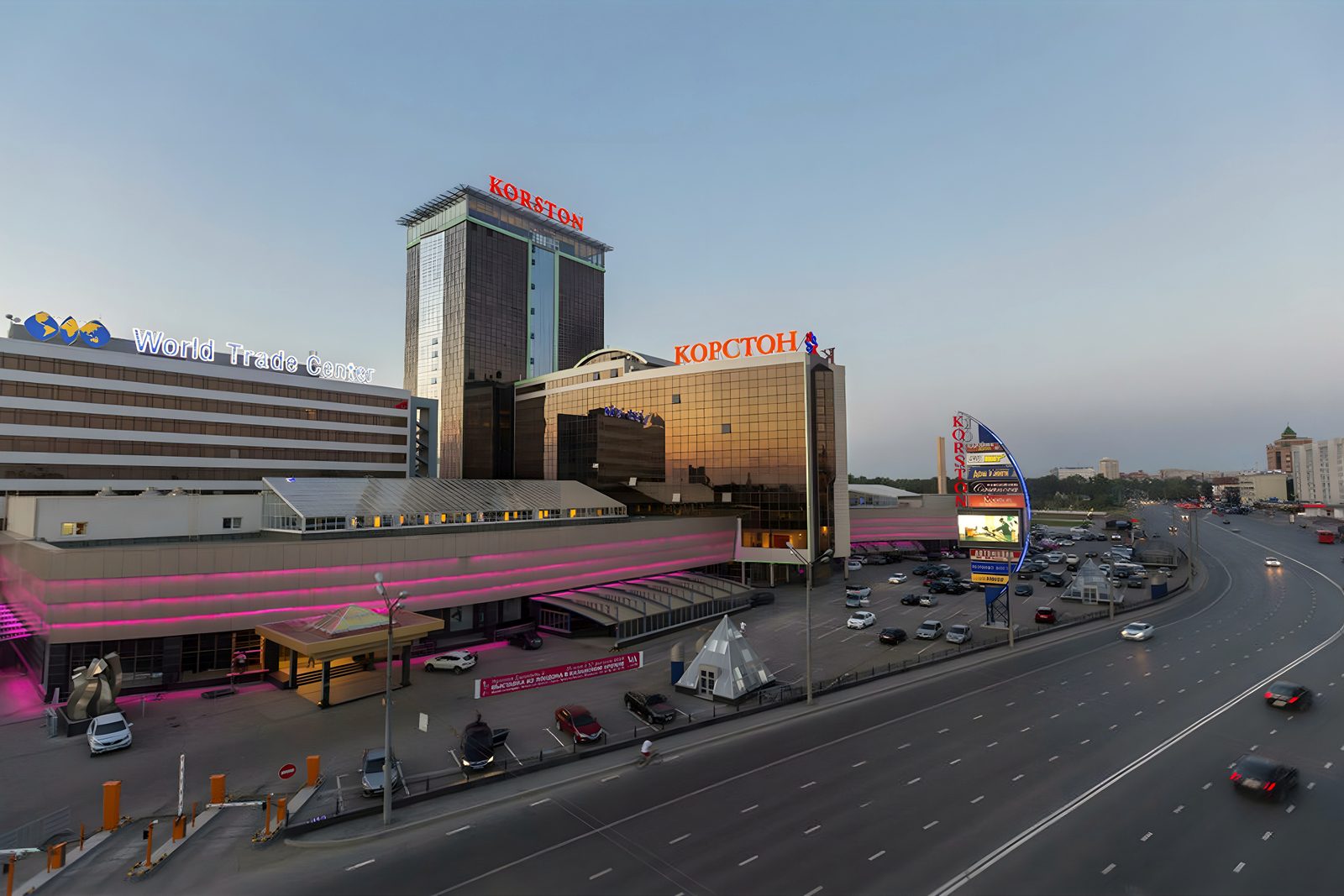 Korston hotel tower and mall beside a multi-lane highway at dusk